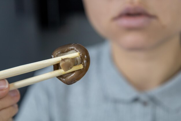 Una chica con una camisa gris en la cocina sostiene un hongo shiitake con palillos Concepto de comida asiática