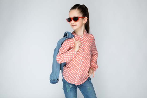 Chica en camisa naranja, gafas y pantalones de mezclilla en gris.