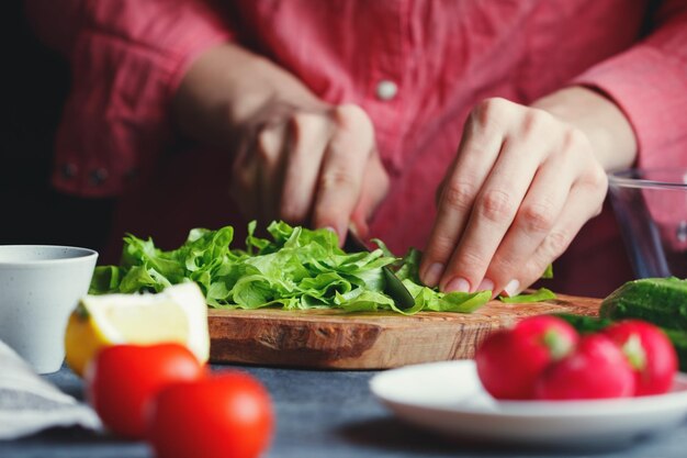 Una chica con una camisa rosa corta una ensalada fresca en una tabla de madera texturizada rodeada de verduras Una serie de fotos sobre la preparación de la ensalada de verduras de verano