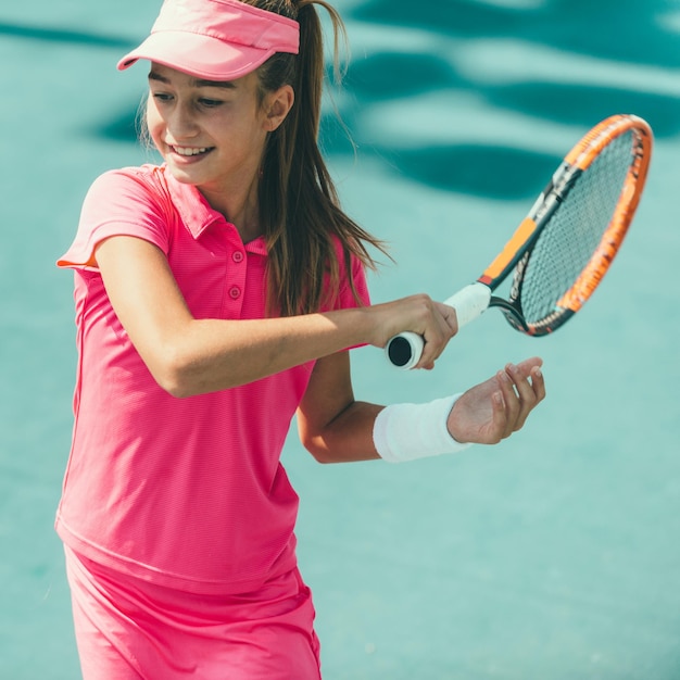 Una chica con una camisa rosa está jugando al tenis y tiene una visera rosa.