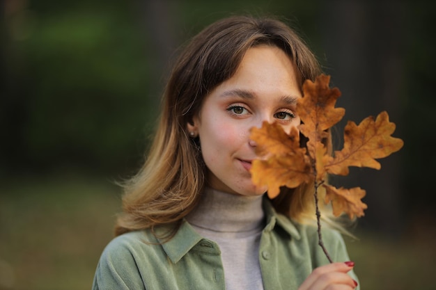 chica con una camisa verde y jeans azules en el bosque de otoño chica sosteniendo una hoja de arce en sus manos