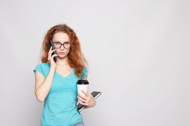 Una chica con una camiseta azul con un teléfono y un café sobre un fondo claro