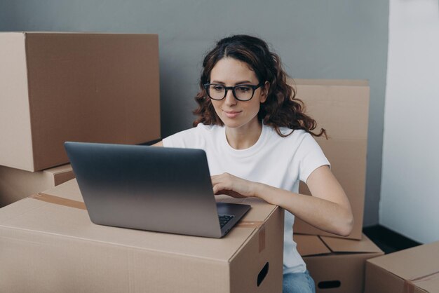 Chica con camiseta blanca y anteojos está enviando mensajes de texto en el servicio de entrega de pedidos de computadora para cajas empacadas