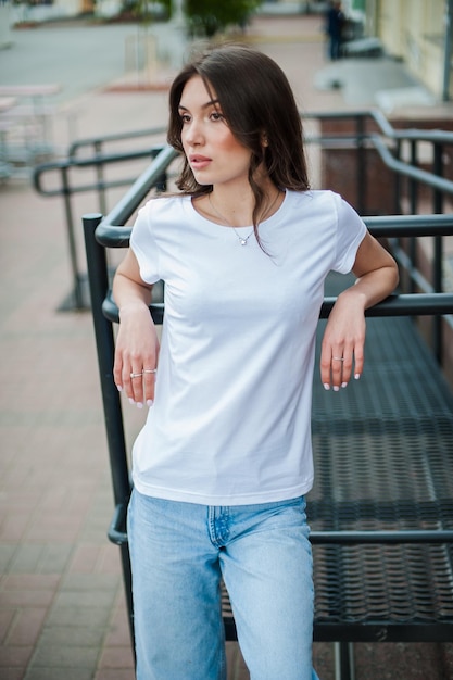 Una chica con una camiseta blanca en blanco apoyó la espalda contra la maqueta de barandilla para la imprenta de camisetas