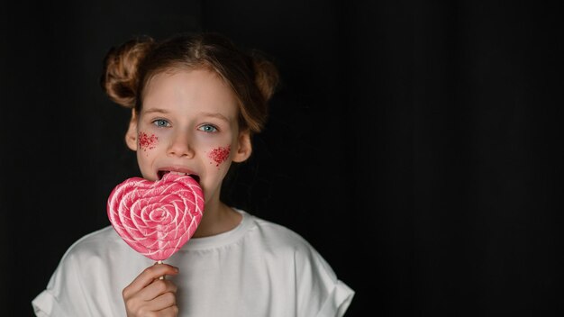 Foto una chica con una camiseta blanca come un caramelo en forma de corazón sobre un fondo negro chica con dos panes