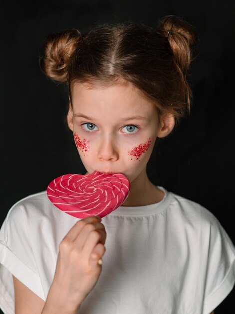 Foto una chica con una camiseta blanca come un caramelo en forma de corazón sobre un fondo negro niños y dulces