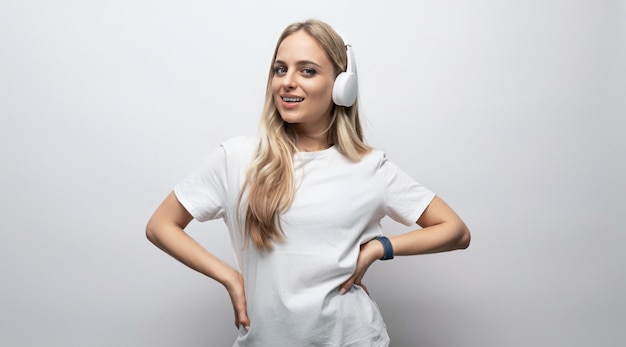 Una chica con una camiseta blanca escucha música con auriculares inalámbricos en un fondo blanco con vacío