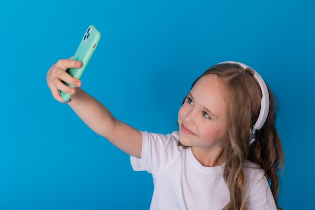 chica con una camiseta blanca y jeans con auriculares en su teléfono inteligente se toma un selfie sentado en el suelo