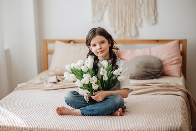 Una chica con una camiseta blanca con un ramo de flores Una chica con una sonrisa tiene tulipanes blancos