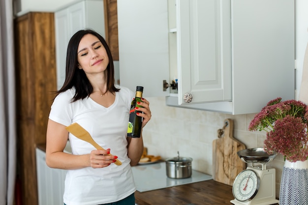 Chica con una camiseta blanca sostiene una espátula de cocina y una botella de aceite de oliva.