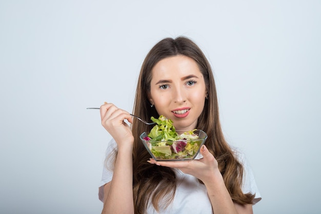 chica con una camiseta blanca sostiene un tazón de ensalada en sus manos y come