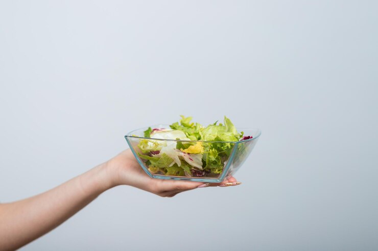 chica con una camiseta blanca sostiene un tazón de ensalada en sus manos y come