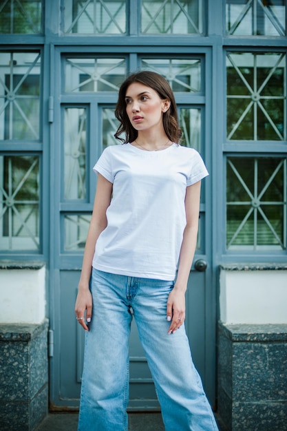 Una chica con una camiseta blanca vacía se para cerca de la maqueta del viento para la imprenta de camisetas