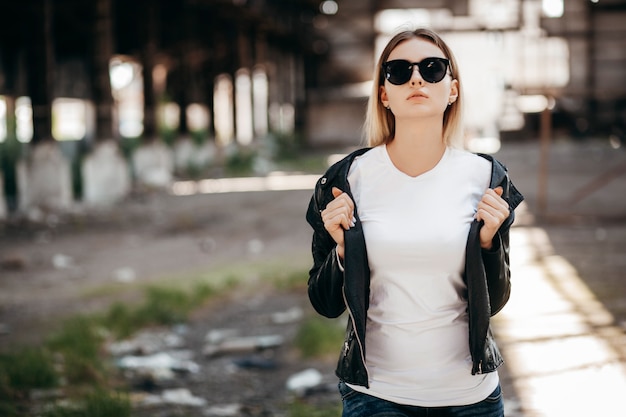 Chica con camiseta, gafas y chaqueta de cuero posando contra la calle