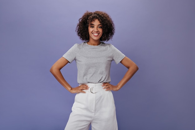 Chica en camiseta gris está sonriendo en la pared aislada