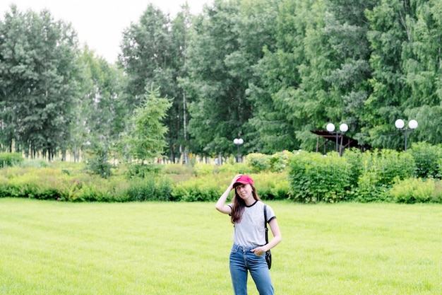 Una chica con una camiseta gris y una gorra roja sobre un fondo de vegetación en el espacio de copia del parque