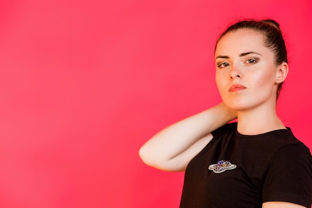 Una chica con una camiseta negra con un broche en forma de planeta con anillos posa sobre un fondo fucsia