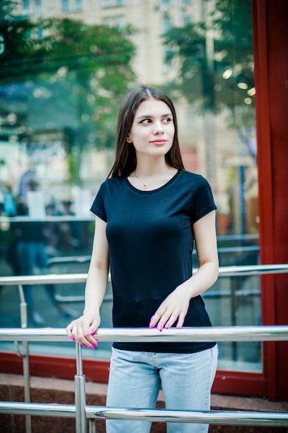 Una chica con una camiseta negra vacía se aferra a la barandilla con una maqueta de una mano para la imprenta de camisetas