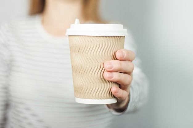 Chica con una camiseta a rayas sostiene una taza de papel con café o té delante de ella.