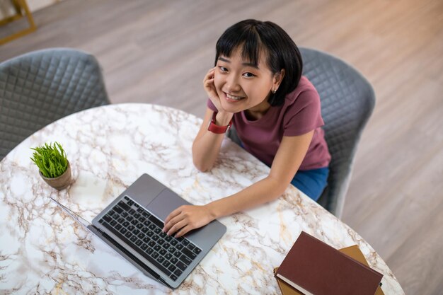 Una chica con camiseta violeta sentada en la laptop y luciendo feliz