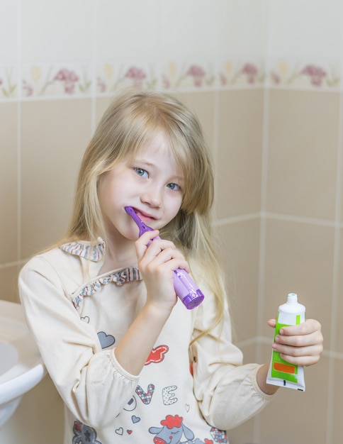 Chica en camisón con un cepillo de dientes eléctrico en el baño.