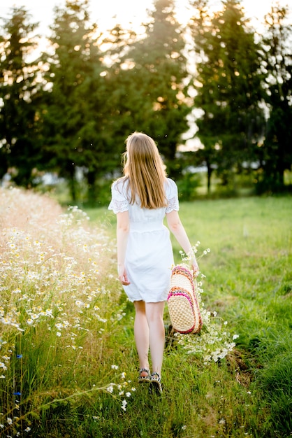 Chica en un campo en la puesta de sol con margaritas