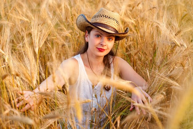 Chica en campo de trigo con vestido blanco y sombrero stetson. Enfoque selectivo.