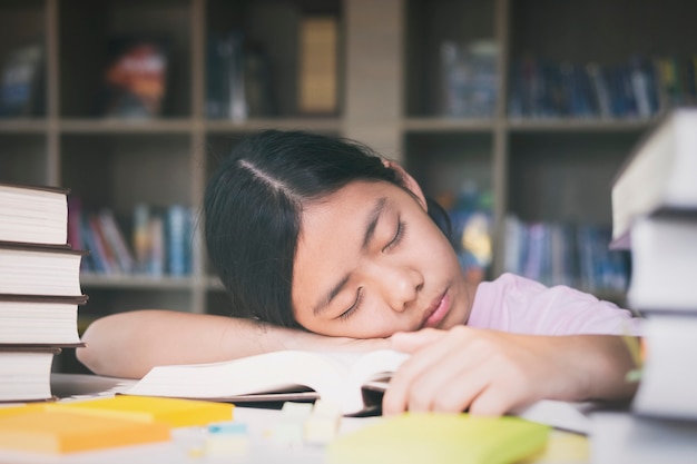 Chica cansada y dormir en libros en la biblioteca. Concepto de educación.