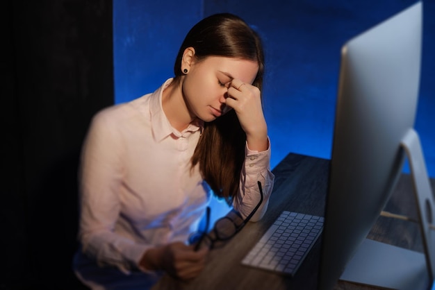 Chica cansada trabaja en la computadora tarde en la noche bebe café los ojos duelen