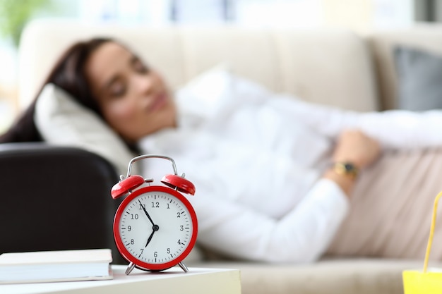 Foto chica está cansada y yace sobre la mesa un despertador