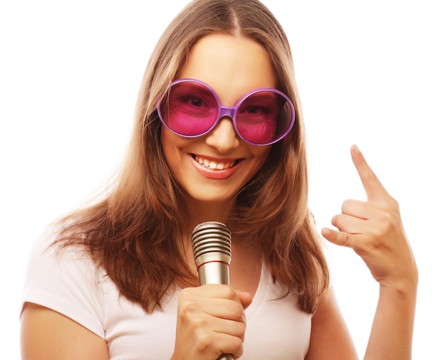 Foto chica cantando feliz mujer de belleza con camiseta blanca y grandes gafas de sol con micrófono sobre fondo blanco ipster styl