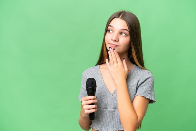 Chica cantante adolescente recogiendo un micrófono sobre un fondo aislado mirando hacia arriba mientras sonríe