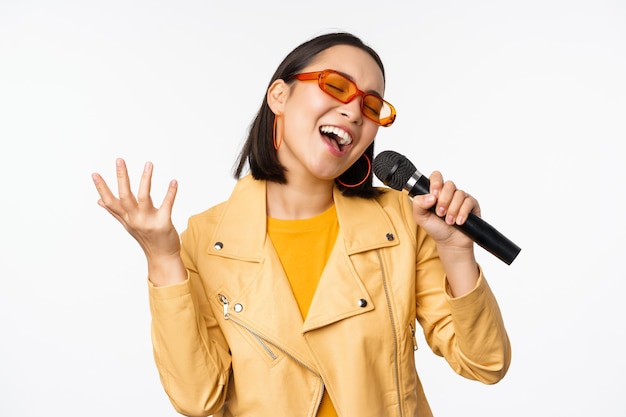 Chica cantante sosteniendo el micrófono interpretando canciones en el karaoke de pie sobre fondo blanco Copiar espacio