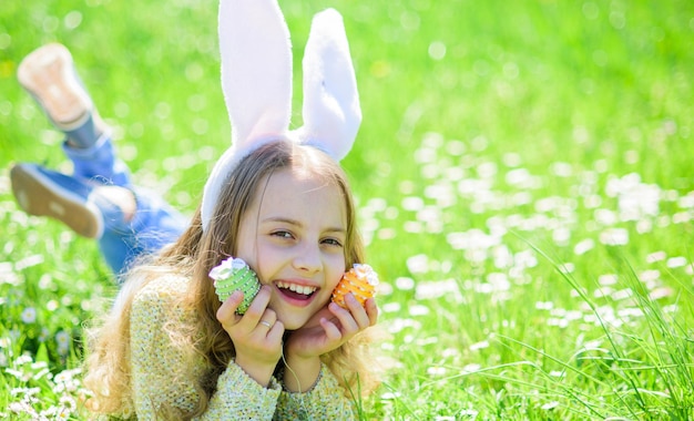 Chica en cara feliz sostiene huevos de Pascua en las manos hierba en el fondo Niño con orejas de conejo acostado en el espacio de la copia del prado