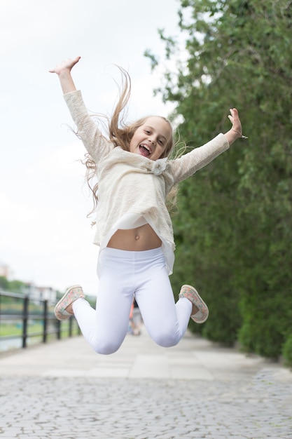 Chica de cara sonriente feliz, naturaleza de fondo. Concepto de felicidad. La muchacha del cabrito con la expresión alegre salta en el día internacional del niño. Niño feliz y alegre disfruta de caminar en el parque.