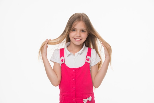 Chica en la cara sonriente posando con el pelo largo, aislado sobre fondo blanco. Niña con cabello largo se ve adorable. Concepto de peinado y cuidado del cabello. A la chica le gusta lucir linda, elegante y a la moda.