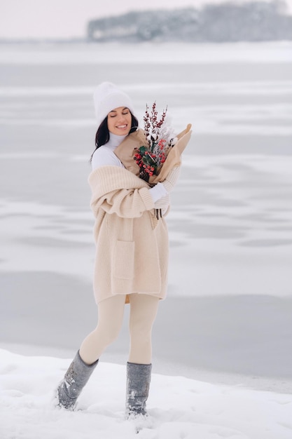 Una chica con un cárdigan beige y flores de invierno camina por la naturaleza en la temporada de nieve Clima invernal