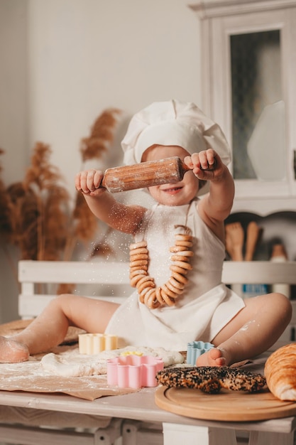 chica carismática con un delantal y un sombrero está sentada y extendiendo la masa