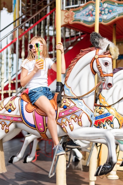 Chica en un carrusel con caballos en una feria