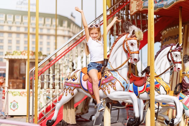 Chica en un carrusel con caballos en una feria