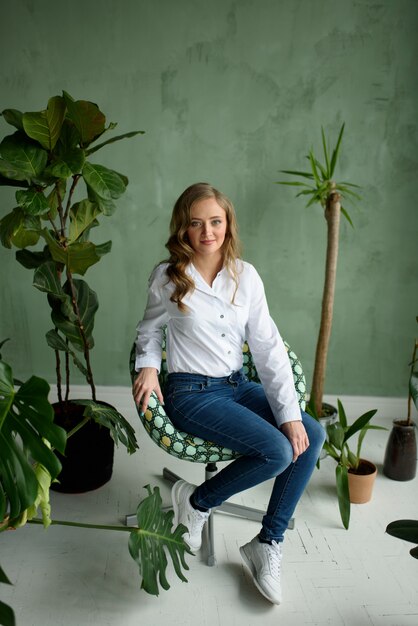 Chica en casa, en la cocina blanca, en ropa verde sentada en una silla verde con un gato en sus brazos