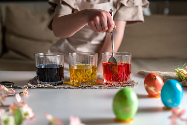 Chica en casa en la cocina tiñe huevos para Pascua