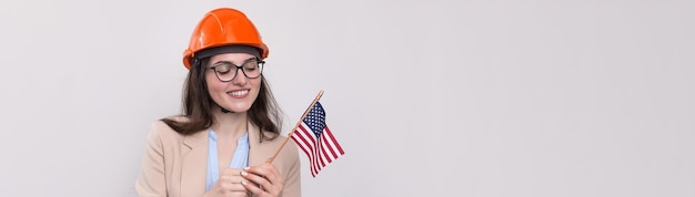 Una chica con un casco de construcción y una bandera americana está feliz con un fondo blanco