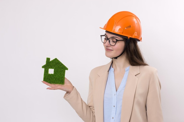 Una chica con casco de construcción sostiene una casa verde. El concepto de vivienda limpia ecológica.