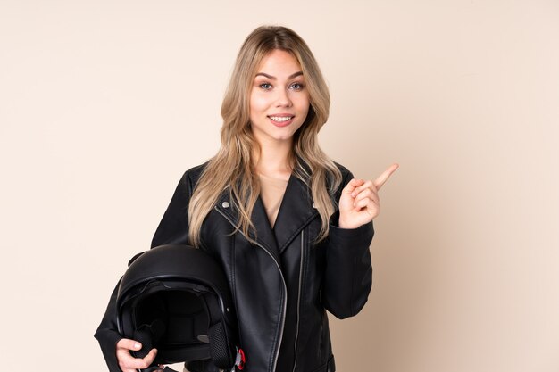 Chica con casco de moto en pared beige apuntando hacia un lado