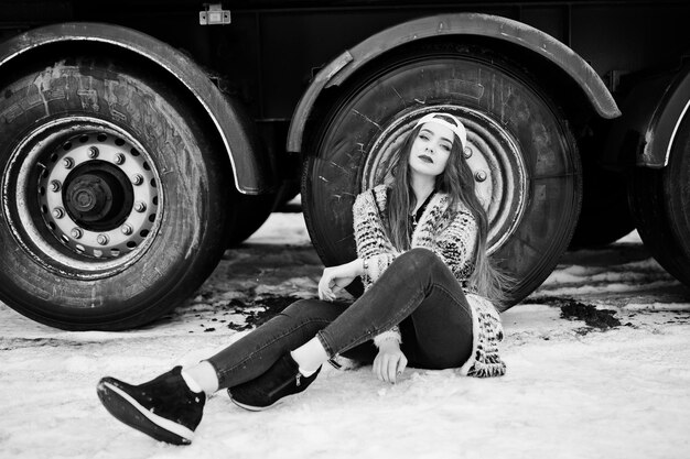 Chica casual elegante morena con gorra sentada contra ruedas de camión