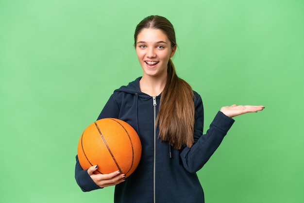 Chica caucásica adolescente jugando baloncesto sobre fondo aislado con expresión facial conmocionada