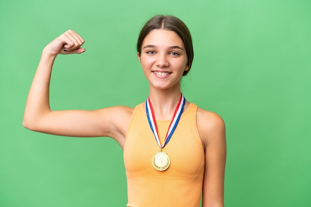 Chica caucásica adolescente con medallas sobre antecedentes aislados haciendo un gesto fuerte