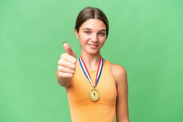 Chica caucásica adolescente con medallas sobre un fondo aislado con los pulgares hacia arriba porque algo bueno ha sucedido