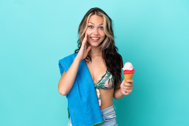 Chica caucásica adolescente sosteniendo helado y toalla aislada de fondo azul con expresión facial sorprendida y sorprendida